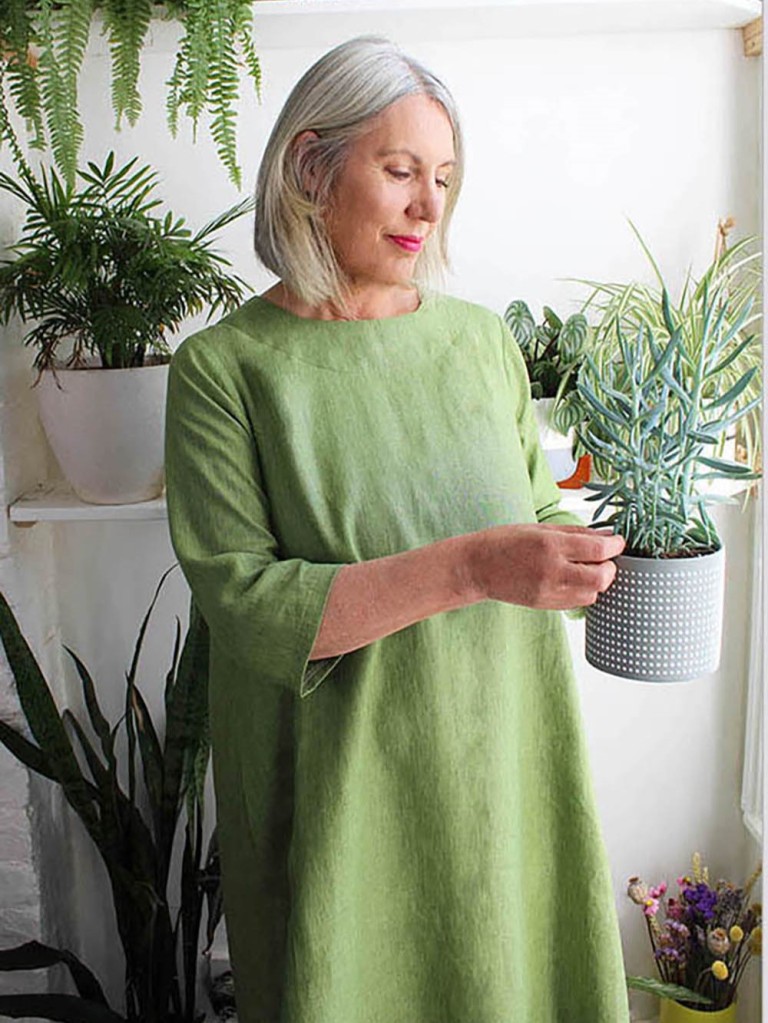Fiona modelling the Orla Trapze Dress in a plain green fabric while holding a plant in a pot